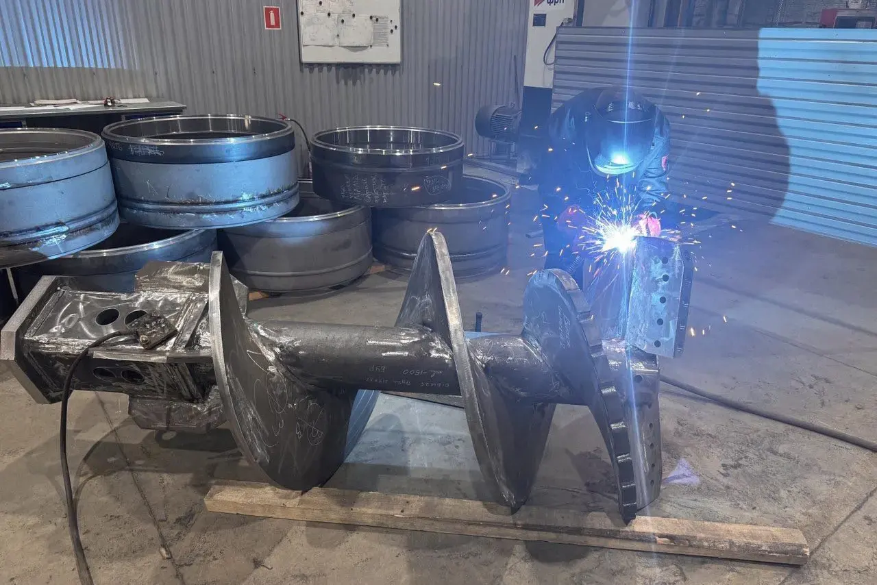 Сварщик варит буровой шнек в цехе